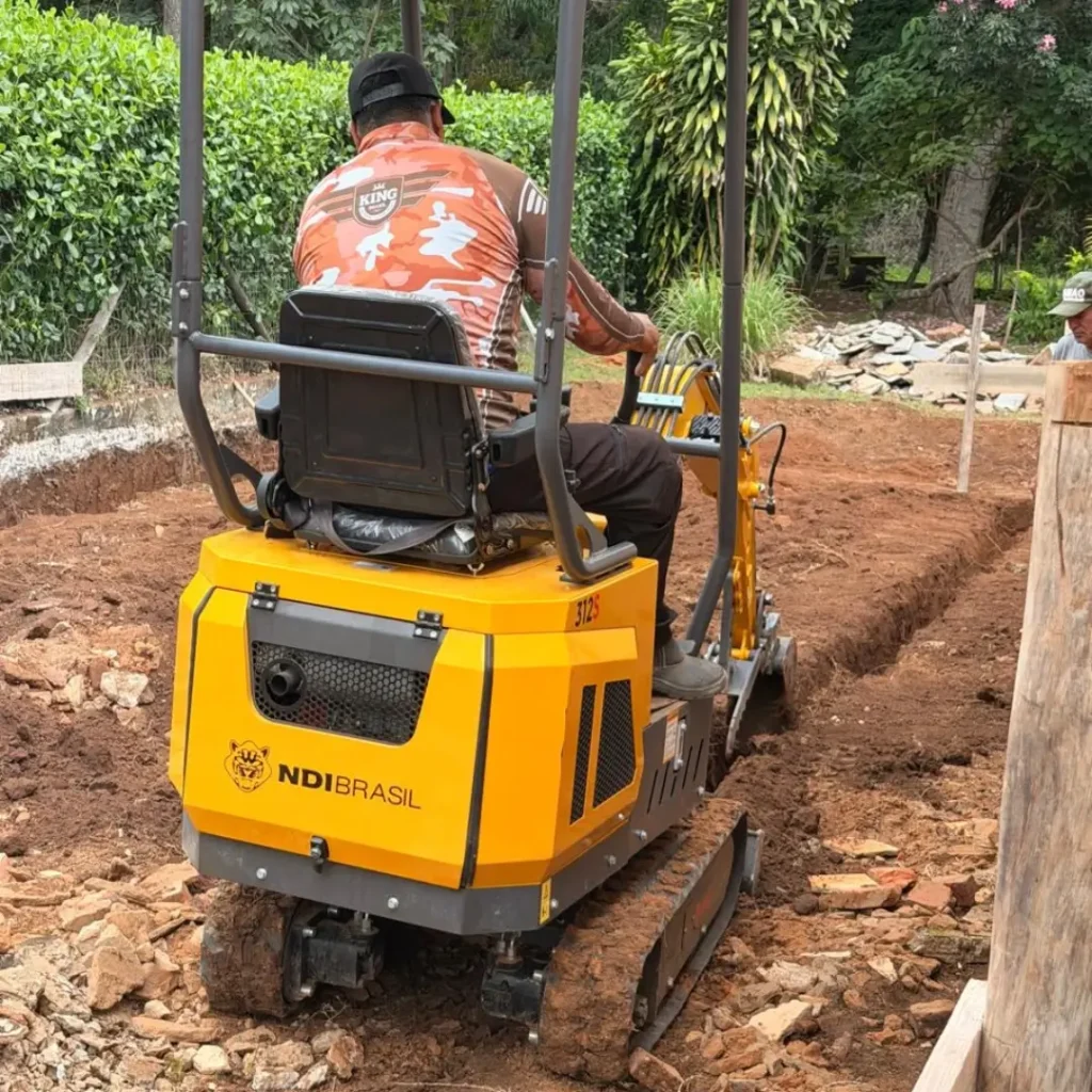 Mini escavadeira própria da LR Construtora realizando escavação de vala técnica em terreno com espaço restrito.